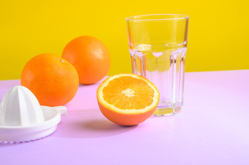 Oranges, a transparent glass and a juicer. Bright background, creative frame, fashion light.