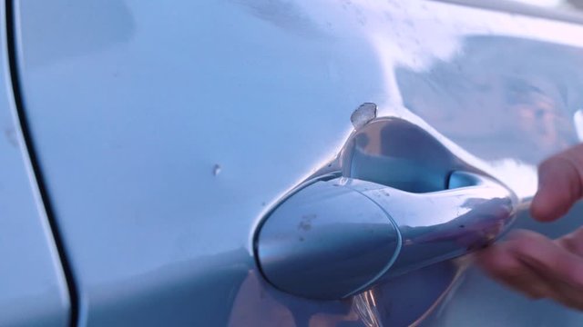 Man spitting on the car door to clean it with the sleeve of his jacket, checking with fingers the paint coating for scratches, close-up. Rusting paint chips on the door handle of the vehicle.