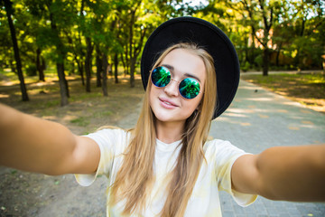 Young attractive playful tourist is making selfie on the phone outside, wearing hat, sunglasses in the street