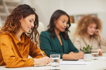 Horizontal eye level shot of three stylish young women making notes during business meeting in modern office