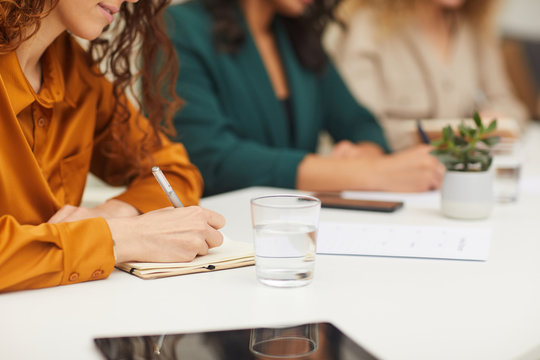 Horizontal shot of three unrecognizable young women sitting together at office table making notes during business meeting