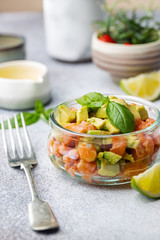 Delicious avocado and raw salmon salad, tartare, served glass jar with lime, light background