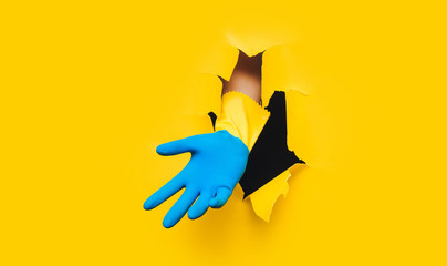 One male hand in yellow and blue household glove. Paper background and torn hole. Copy space. Guest worker concept.