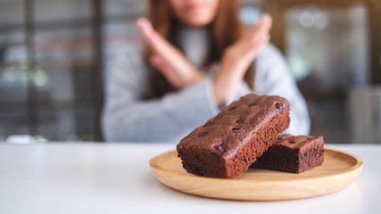 A woman making arms cross sign to refuse a brownie cake in wooden plate