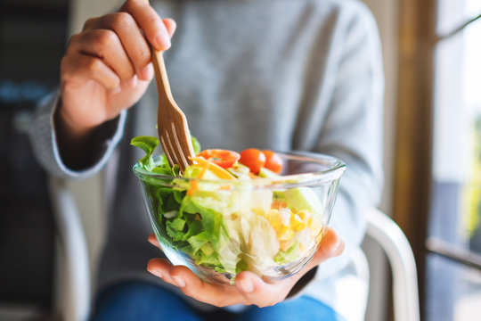 Closeup image of a woman eating and holding a bowl of fresh mixed vegetables salad by fork
