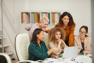 Fototapeta premium Group of five positive stylish women using laptop to work on project during business meeting horizontal shot