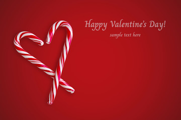 Two red and white candy canes in the shape of heart on a red background.