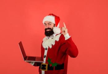 Santa Claus working with laptop. Bearded businessman in Santa costume holds laptop and pointing up. Holidays. Merry Christmas and Happy New Year. Santa holds laptop. Digital device.