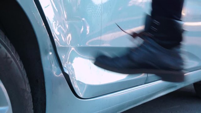 Bad man is kicking the car door with anger in the street, close-up. Revenge of neighbor for improper parking, insurance fraud due to expensive repairs.