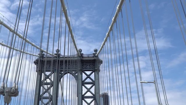 Driving over the Manhattan Bridge, low angle shot and wide lens used, steel suspension cables passing by quickly against the blue sky
