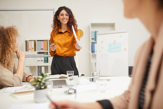 Attractive businesswoman with curly hair giving explanation of import of new business strategy at meeting, horizontal shot