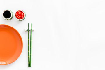 Tableware for sushi and rolls. Plate, chopsticks, small bowls with ginger and sause on white background top-down copy space