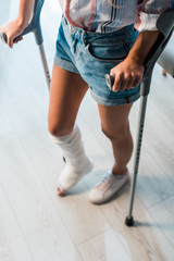 cropped view of fractured woman holding crutches while standing in clinic
