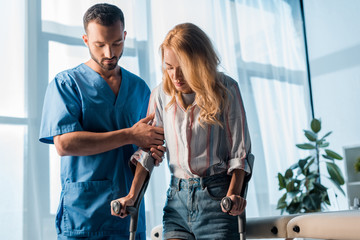 handsome doctor standing near woman with crutches