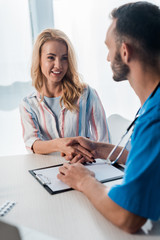 Obraz premium selective focus of smiling woman shaking hands with bearded doctor in clinic