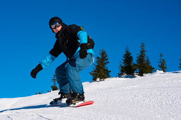 Fototapeta na wymiar Snowboarder Riding Red Snowboard in Mountains at Sunny Day. Snowboarding and Winter Sports