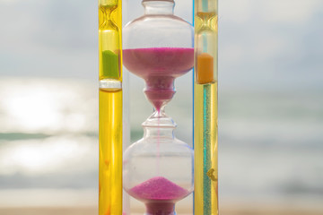 The hourglass passing time on the beach The hourglass in front of the bright blue sky with white...