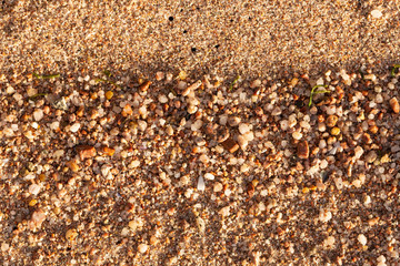 Small pebbles form the background of the sea shore. Coarse multicolor sand.