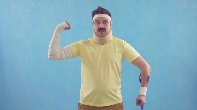 Funny mustachioed man after a sports injury with crutches poses for the camera standing on a blue background