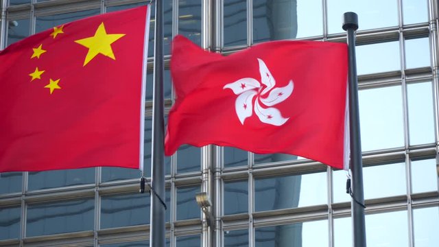 Hong Kong and China Flags Waving in a Downtown Financial District Against modern Bank Office Building