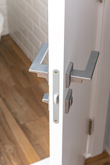 Modern chrome door handle and lock on white wooden door. Close-up elements of the modern interior of the apartment. Ajar white door.
