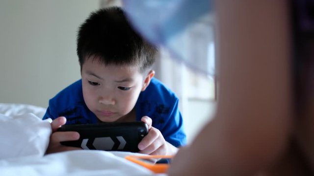 asian chinese boy playing smartphone on bed, kid use phone and play game, addicted game and cartoon, 