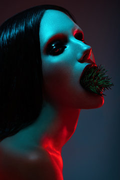 Portrait of attractive brunette woman with fir twig in opened mouth posing on dark studio background 