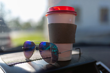 White paper coffee Cup and sunglasses on the dashboard of the car. Paper Cup with hot tea and glasses on the dashboard of the SUV close up against the background of a blurred traffic jam