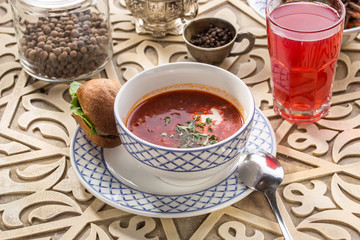 Red beetroot soup borshch with bread bun and sour cream on oriental wooden table