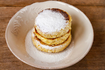Russian traditional breakfast cottage cheese pancake in plate with sugar powder on wooden background