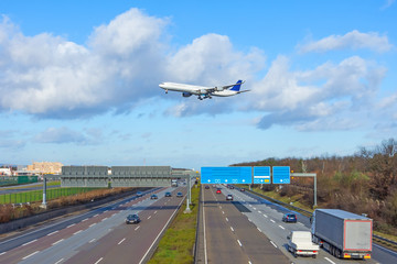 Landing airplane flies over a high-speed highway with cars in the city. Travel concept by air or ground.