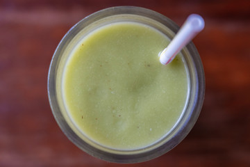 Glass of avocado smoothie with drinking straw on wooden background, top view