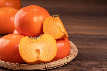 Fresh, beautiful orange color persimmon kaki on bamboo sieve over dark wooden table. Seasonal, traditional fruit of Chinese lunar new year, close up.