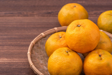 Fresh, beautiful orange color tangerine on bamboo sieve over dark wooden table. Seasonal, traditional fruit of Chinese lunar new year, close up.