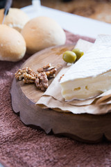 vertical photo, brie cheese next to lie nuts and olives on a wooden board next to fresh buns