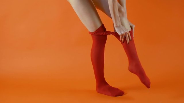 Female model with perfect long legs is wearing red tights on in studio over bright orange background
