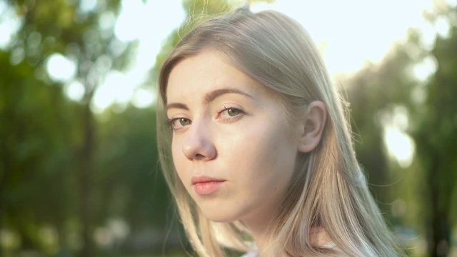 Portrait of young beautiful blonde woman with a lovely look a looking at camera outdoors Close up sunshine lens flare