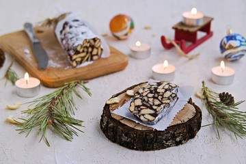 Dessert, chocolate salami with cookies and cashews in the New Year and Christmas style on a wooden board on a light concrete background. Desserts without baking.