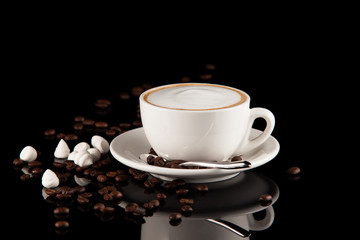 Classic white cappuccino Cup on dark background. Coffee beans, meringues and reflection.