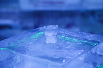 A glass for vodka and other drinks made of ice stands on an ice block.