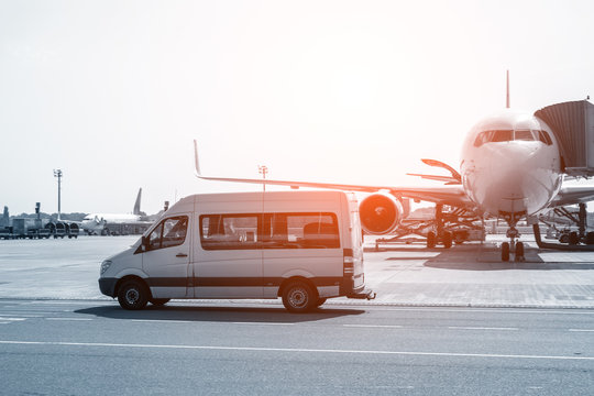 White VIP Service Van Running On Airport Taxiway With Big Passenger Airplane On Background. Business Class Service At Airport. Security Intelligence Agency Hurrying At Airfield