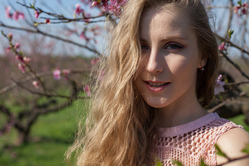 Beautiful blonde woman in pink dress walks through the flowering garden spring
