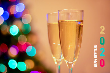 Blurred christmas tree, two glasses with sparkling wine champagne and numbers 2020 for the upcoming year