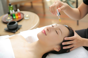 Obraz na płótnie Canvas Beautician drops a drop of essential oil on the face of an Asian beauty for a spa