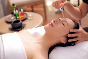 Obraz na płótnie Canvas Beautician drops a drop of essential oil on the face of an Asian beauty for a spa