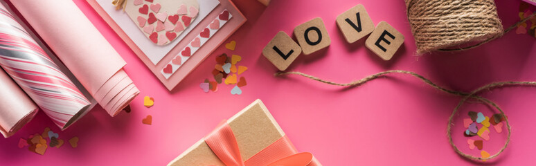 top view of valentines decoration, wrapping paper, twine, gift, greeting card and love lettering on wooden cubes on pink background, panoramic shot