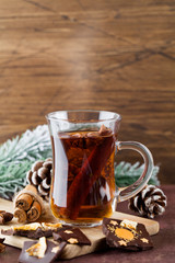 Winter hot tea with cinnamon, anise, chocolate with fruit, cone and christmas tree branch on wood brown background.