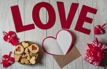 The Concept Of Valentine's Day. Love letter. A blank sheet of paper, an envelope, a gift box, homemade cookies, wooden letters and red hearts on a light wooden background.