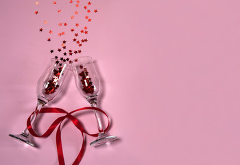 The Concept Of Valentine's Day. Two narrow empty wine glasses tied with a red ribbon, and stars on a pink background. Free space for your text.