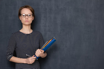 Portrait of serious focused girl with glasses, holding folders and pen
